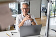 © peter scholl/Westend61 - Smiling male entrepreneur with laptop sitting at desk in open plan office