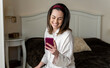 © VITTA GALLERY/Westend61 - Cheerful young woman using smart phone while sitting on bed