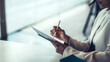 © amnaj - Close up of a businesswoman holding a pen working on a tablet at the office.