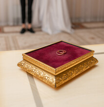 Two Gold Wedding Rings On A Stand On The Table In The Registry Office, In The Background The Bride And Groom. The Concept Of Marriage, Family, Wedding, Love. Selective Focus