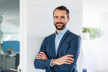 Confident Male Entrepreneur Smiling While Standing With Arms Crossed At Office