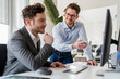 © Daniel Ingold/Westend61 - Smiling male colleague discussing with businessman over computer in office