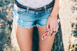 Close up image on woman legs in blue jeans shorts standing in front of a tree and holding accessory.