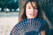 Vertical portrait of a beautiful brunette young woman with blue hand fan.