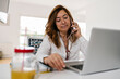 © Ezequiel Gim√©nez/Westend61 - Female entrepreneur talking on smart phone while sitting with laptop on desk at home