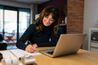 © Ezequiel Gim√©nez/Westend61 - Smiling woman with laptop writing in paper while sitting at home