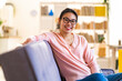 © Giorgio Fochesato/Westend61 - Young woman wearing eyeglasses sitting on sofa at home