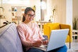 © Giorgio Fochesato/Westend61 - Smiling young woman holding credit card while sitting with laptop at home