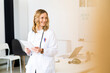 © Giorgio Fochesato/Westend61 - Smiling female healthcare worker with tablet leaning on desk while standing in medical clinic