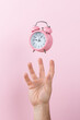© Plutmaverick - Pink alarm clock levitate on a man's hand, on a pink background. Copy space.