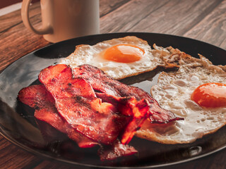 Canvas Print - Closeup shot of breakfast with a coffee, tasty meats, and eggs on the black plate