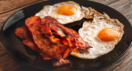 Wall Mural - Closeup shot of breakfast with tasty meats and eggs on the black plate