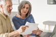© insta_photos - Older mature couple checking bank documents using laptop at home. Senior mid age retired man and woman reading paper bills, calculating pension or taxes, planning retirement finances, doing paperwork.