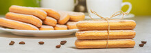 Italian savoiardi biscuits or ladyfingers cookies on a plate and in a stack, a jug of milk in the background, banner. Selective focus