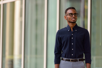 Wall Mural - Portrait of handsome African businessman outdoors in city smiling and thinking