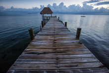 A Long Empty Wooden Dock Juts Out Into The Caribbean Sea Just Before Dawn On The Mainland Of Belize.