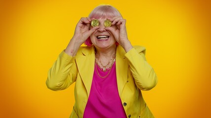 Cheerful senior old stylish granny woman in jacket showing golden bitcoins. Achievement career wealth, cryptocurrency investment, mining, future technology. Elderly grandmother fooling, making faces