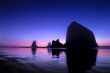 The Sun Sets Behind Haystack Rock At Cannon Beach, Oregon, As The Planet Venus Hovers On The Horizon.