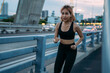 Sporty Asian female athlete in sportswear running in evening during sunset at bridge for a healthy and fit body. Young woman jogging in city