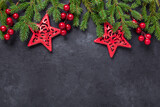 Fototapeta Na ścianę - Christmas background with fir tree, holly and red stars on dark stone background. Top view Copy space