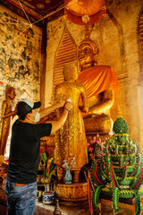 Man in black wear mask paste gold on back of buddha statue in Thailand temple or wat. The spirituality traditional architecture of faith and religion of Asia culture.