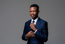 Portrait Of Young Handsome African Man Wearing Formal Business Suit Holding Necktie And Looking At Camera Isolated On Studio Gray Background