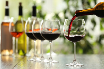 Pouring red wine from bottle into glass on wooden table