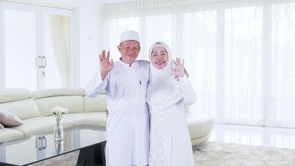 Wall Mural - Happy Muslim old couple waving hands in living room