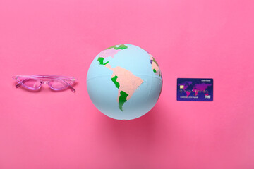 Globe with sunglasses and credit card on color background