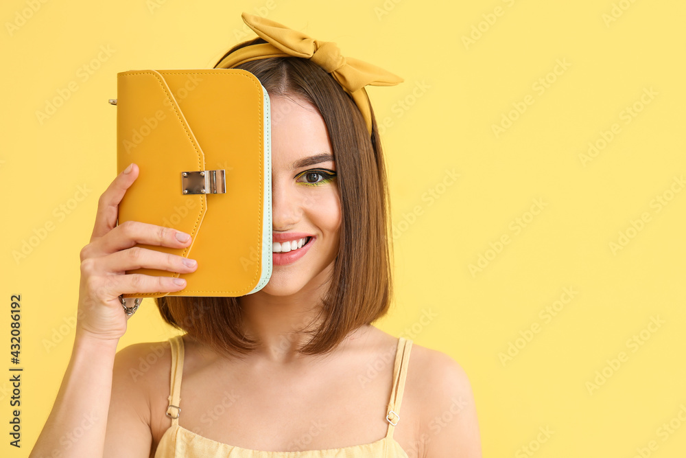 Stylish young woman with bag on yellow background