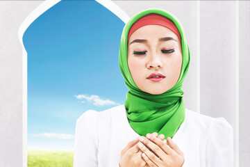 Wall Mural - Asian Muslim woman in a veil sitting while raised hands and praying