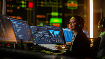 Fototapete - Multiethnic Female IT Technical Support Specialist Talking with a Client in Headphones and Working on Desktop Computer in Monitoring Control Room with Big Digital Screens with Server Blockchain Data.