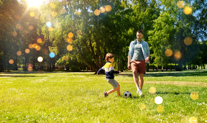 family, fatherhood and people concept - happy father and little son with ball playing soccer at summer park