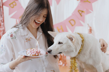 Wall Mural - Dog birthday party. Happy woman celebrating dog first birthday with donut and candle in festive room