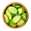 Slices of snack cucumbers, in a wooden bowl. Heap of diagonally cut fresh, small, young and whole cucumber fruits. Cucumis sativus, a vegetable. Close-up, from above, isolated, over white, food photo.