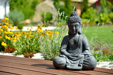 A Closeup Of A Small Buddha Statue In A Garden With A Blurry Background