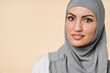 Close up cropped portrait of a beautiful young muslim Middle Eastern islamic arabian woman in grey hijab isolated over beige background. Islam confession religion