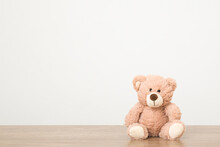 Smiling Brown Teddy Bear Sitting On Wooden Table At Light Gray Wall Background. Closeup. Front View. Empty Place For Text, Quote Or Saying.