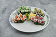 Set of maki sushi rolls with salmon, tuna, avocado and cucumber in a white plate on a gray background. Japanese food