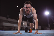 Caucasian Male Athlete With Prosthetic Leg In Starting Position For Running On The Track At Night