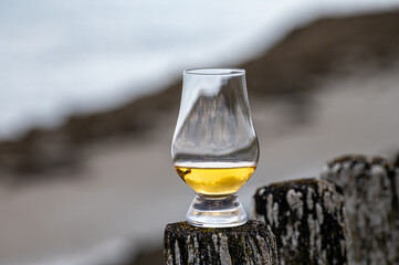 Tasting of dram single malt scotch whisky on seashore in Scotland, old wooden pole with whisky glass