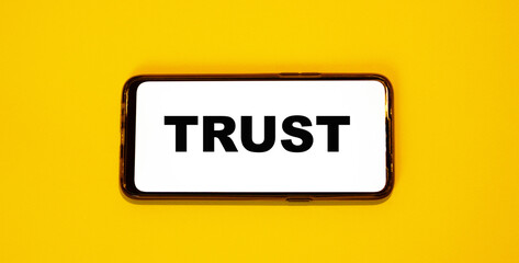 TRUST concept on a smartphone screen on a yellow background. The concept of trust in modern technologies and ideas.