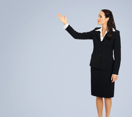 Sticker - Full body of happy smiling woman in black confident suit, showing at copy space. Business concept. Isolated over grey background. Brunette businesswoman.