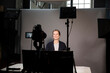 © Maskot - Smiling female entrepreneur video recording on television camera in office
