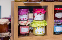 Jam, Curd And Honey Jars For Sale On A Shelf At A Fayre With Colourful Lid Decoration