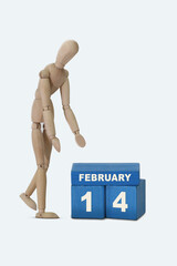 day of the month 14 February calendar . A calendar date on blue cubes and a wooden man standing next to it. White background