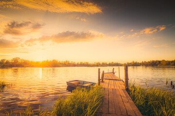 Sunset over the lake with a wooden bridge and boat. View from the shore