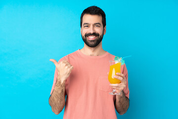 Young man over holding a cocktail over isolated blue background with thumbs up gesture and smiling