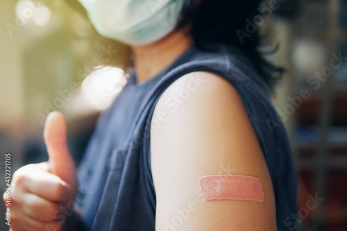 Close-up adhesive bandage on unrecognized person\'s arm after injection of vaccine, people in face mask received a coronavirus COVID-19 vaccine and giving thumb up to recommended inoculation vaccine.