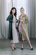 © Alex Li - Young girls stands in the studio on the background of curtains. Fashionable modern raincoats are worn over the dresses. Beautiful healthy teeth are visible.